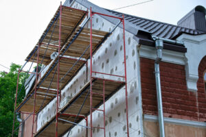 Building facade under renovation works with construction scaffolding frame. Wall insulation with styrofoam sheets for energy efficient home.