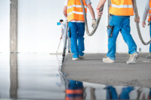Crop men with hose working in team and pouring self leveling concrete floor in building under site