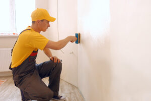 Man applying wallpaper glue using a brush. Construction worker making renovation in a living room.